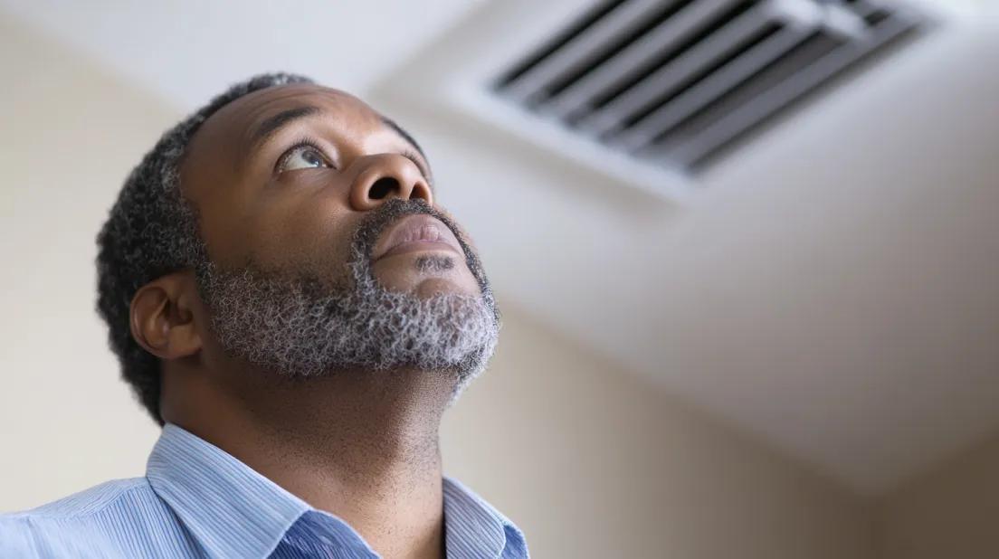 Man looking up at air vent because of AC burning smell
