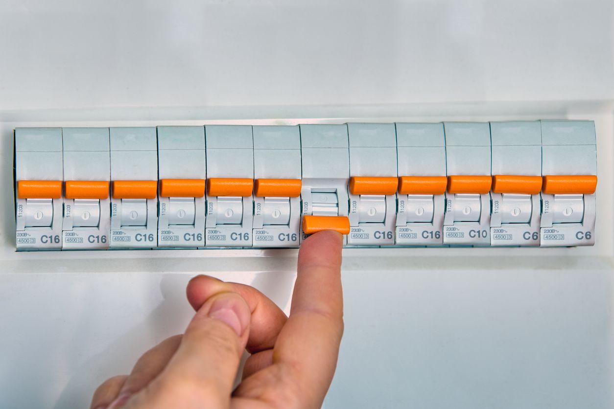 Person switching on circuit breaker on panel board after it tripped due to overcurrent.