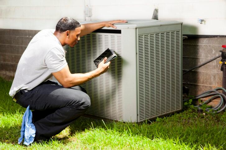 Home inspector, repairman, adjuster examines air conditioner units at a customer home.  He is using his digital tablet to record results.