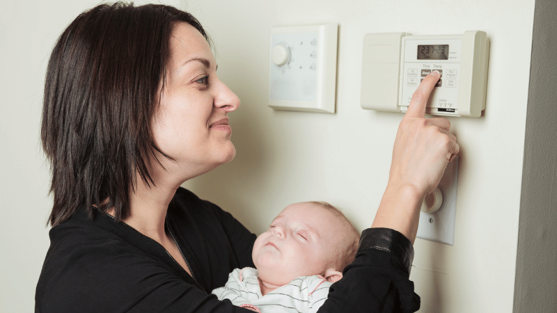 woman and baby adjusting thermostat